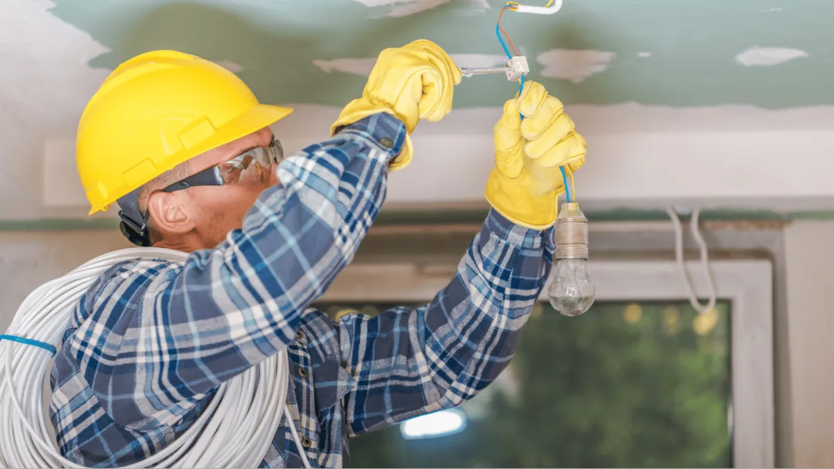 Electrician installing light fixture indoors.